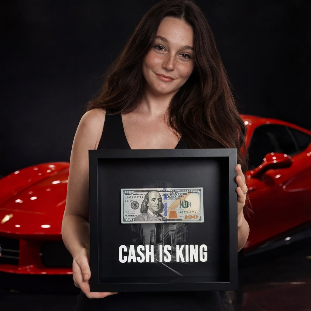 Fiatal nő egy "CASH IS KING" feliratú, dollárköteges képkeretet tart egy piros sportautó előtt.