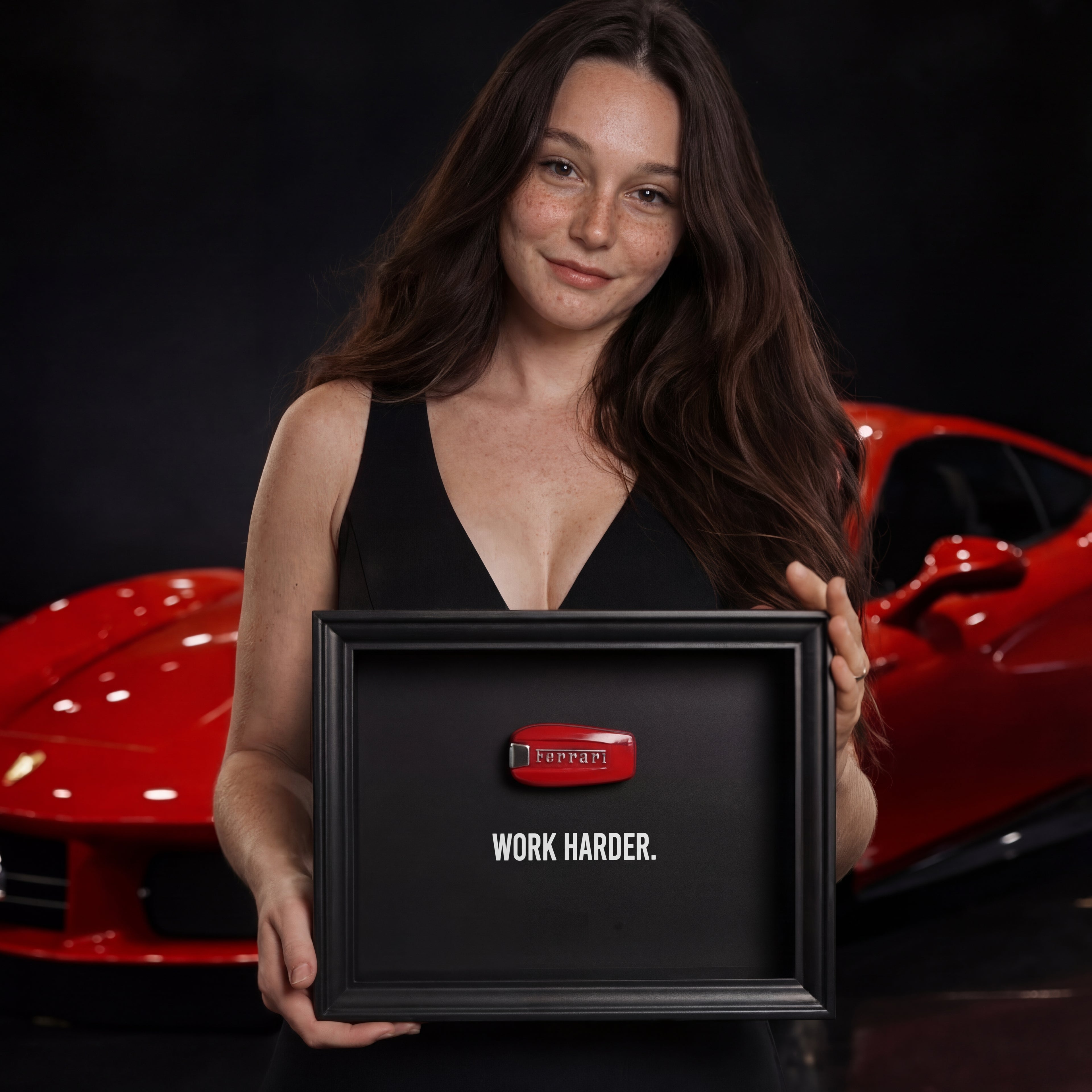 Hosszú barna hajú, mosolygó nő egy fekete képkeretet tart. A keretben egy piros 3D-s Ferrari autókulcs és a "WORK HARDER." felirat látható. A háttérben egy piros luxusautó parkol.